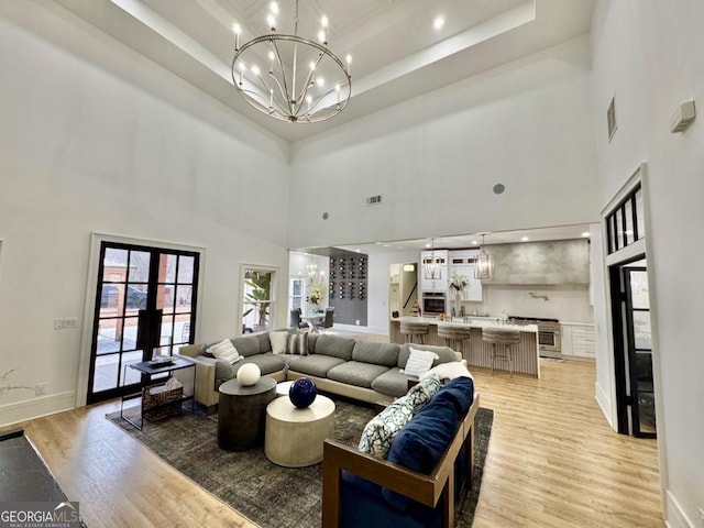 living room with a chandelier, light wood-type flooring, and a tray ceiling