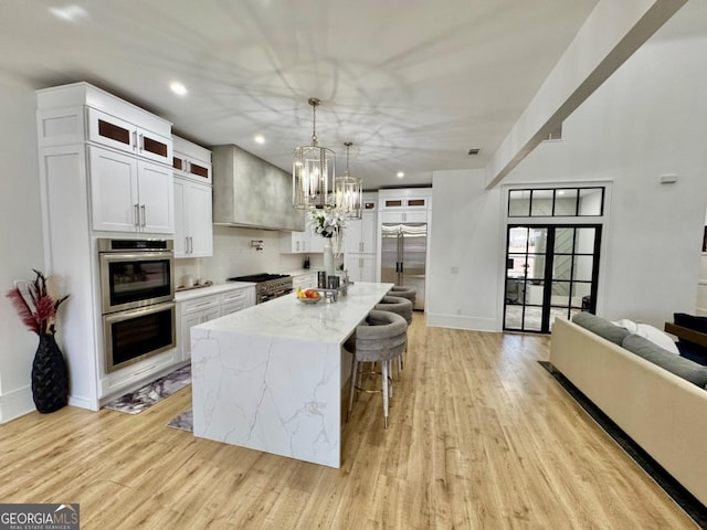 kitchen with premium appliances, white cabinets, custom exhaust hood, light stone countertops, and light wood finished floors