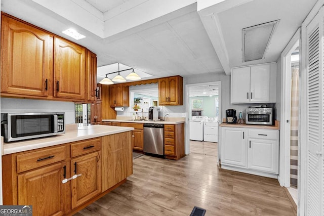 kitchen with stainless steel appliances, light countertops, brown cabinetry, light wood-style floors, and washer and dryer