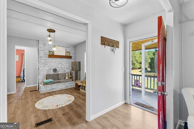 doorway to outside featuring a brick fireplace, wood finished floors, visible vents, and baseboards