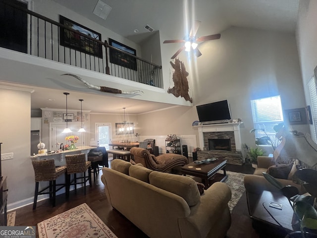 living area with visible vents, dark wood finished floors, a ceiling fan, ornamental molding, and a stone fireplace