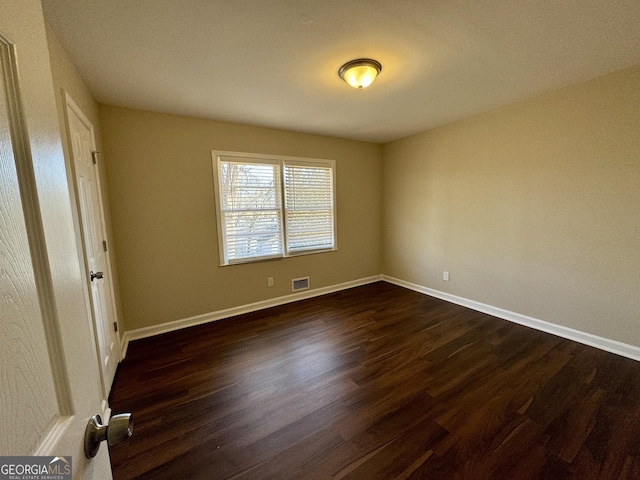 unfurnished bedroom featuring dark wood-style flooring, visible vents, and baseboards