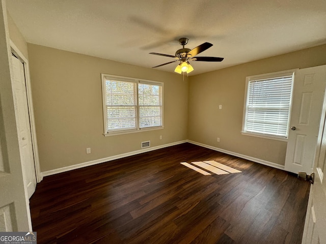 unfurnished bedroom with visible vents, multiple windows, baseboards, and dark wood finished floors