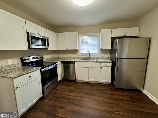 kitchen with light stone counters, stainless steel appliances, dark wood-type flooring, white cabinets, and a sink