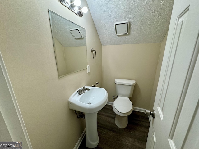 half bath featuring toilet, vaulted ceiling, a textured ceiling, wood finished floors, and baseboards