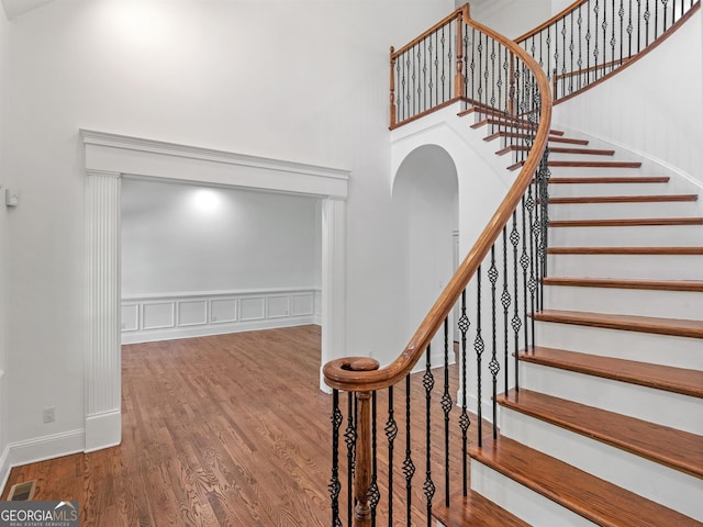 staircase with wainscoting, visible vents, a towering ceiling, and wood finished floors