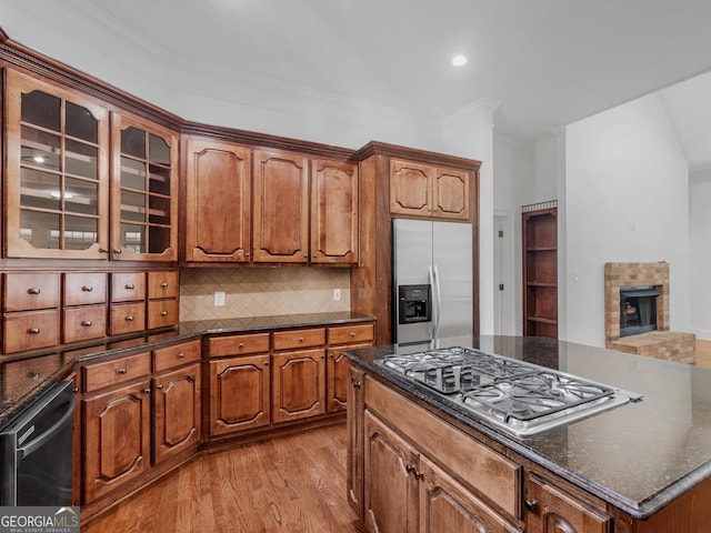 kitchen with brown cabinets, light wood finished floors, stainless steel appliances, decorative backsplash, and glass insert cabinets