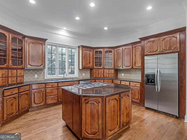 kitchen with a center island, appliances with stainless steel finishes, ornamental molding, a sink, and light wood-type flooring