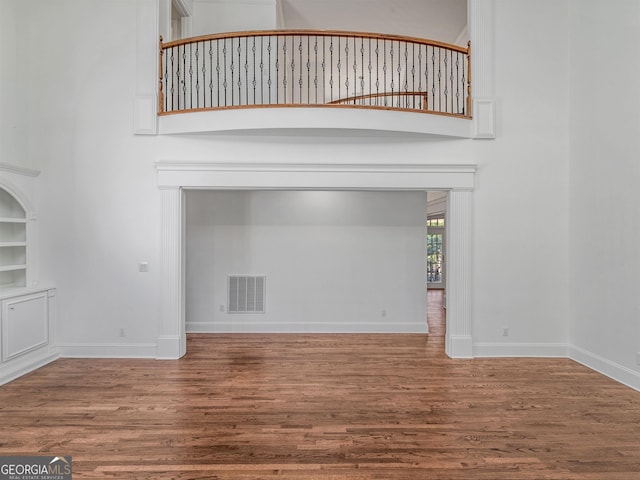 unfurnished living room with a high ceiling, wood finished floors, visible vents, and baseboards