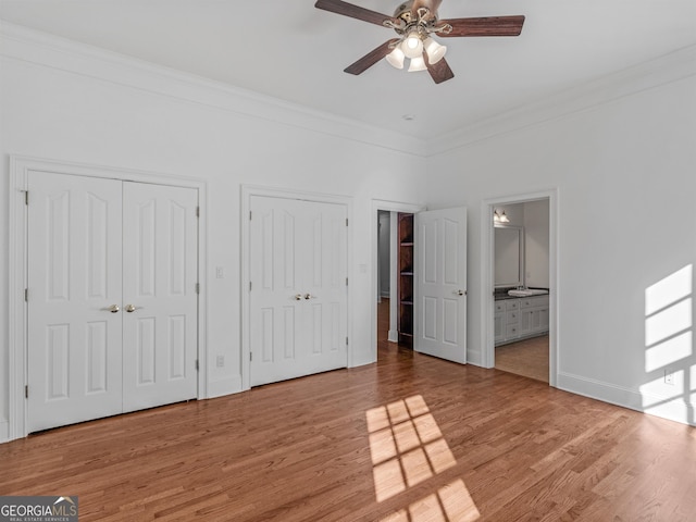 unfurnished bedroom featuring ornamental molding, light wood finished floors, and two closets