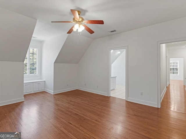 additional living space featuring light wood-type flooring, baseboards, visible vents, and lofted ceiling