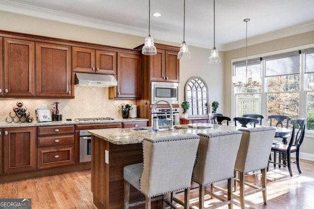 kitchen with under cabinet range hood, stainless steel appliances, a sink, and a kitchen breakfast bar