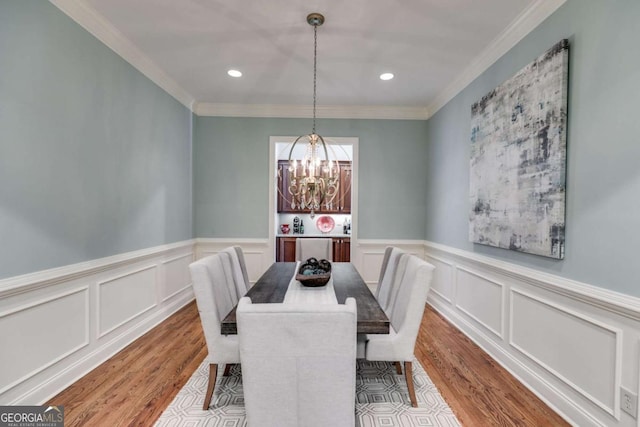 dining space featuring wood finished floors, an inviting chandelier, crown molding, a decorative wall, and recessed lighting