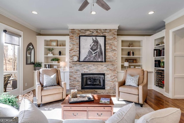 living area with crown molding, baseboards, wood finished floors, and a stone fireplace