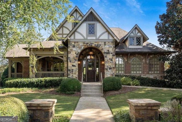 tudor home featuring stucco siding, a shingled roof, a front yard, and brick siding