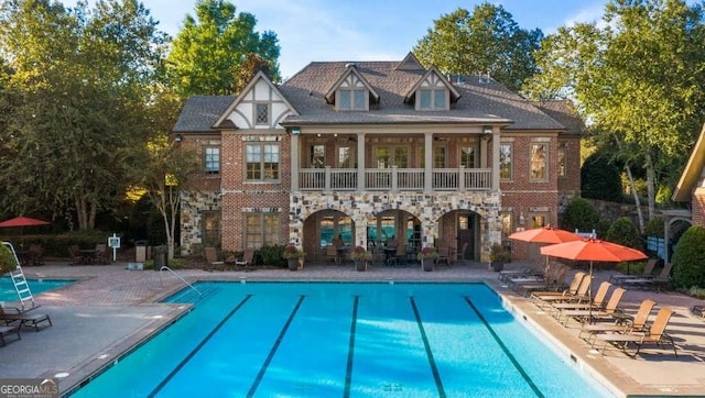 rear view of property featuring stone siding, a patio area, a balcony, and a community pool