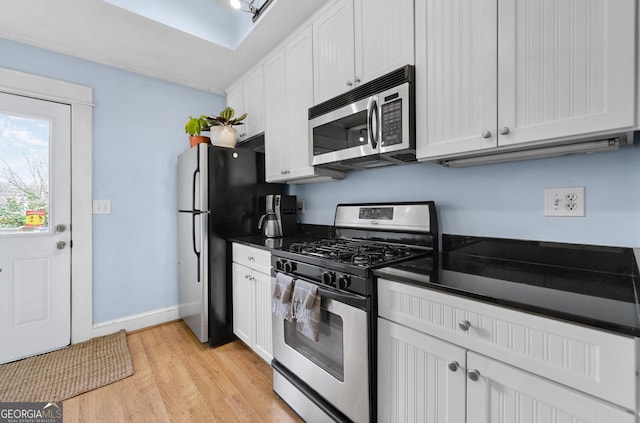 kitchen featuring appliances with stainless steel finishes, dark countertops, white cabinets, and light wood-style flooring