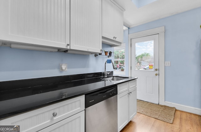 kitchen featuring dark countertops, light wood-style flooring, stainless steel dishwasher, white cabinets, and a sink