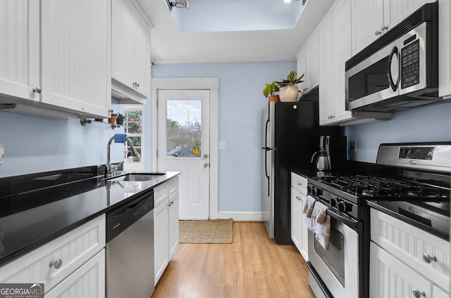 kitchen with dark countertops, appliances with stainless steel finishes, white cabinets, a sink, and light wood-type flooring