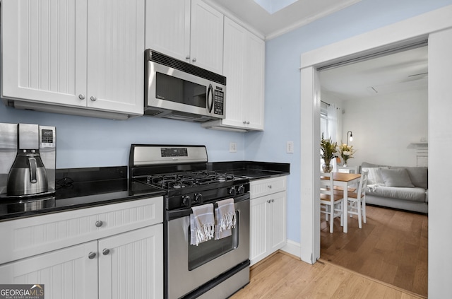 kitchen featuring light wood-style flooring, stainless steel appliances, baseboards, white cabinets, and dark countertops