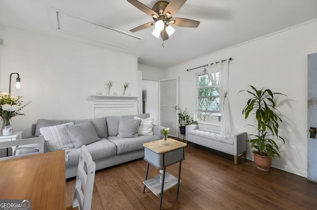 living area with attic access, dark wood-style flooring, ornamental molding, and a ceiling fan