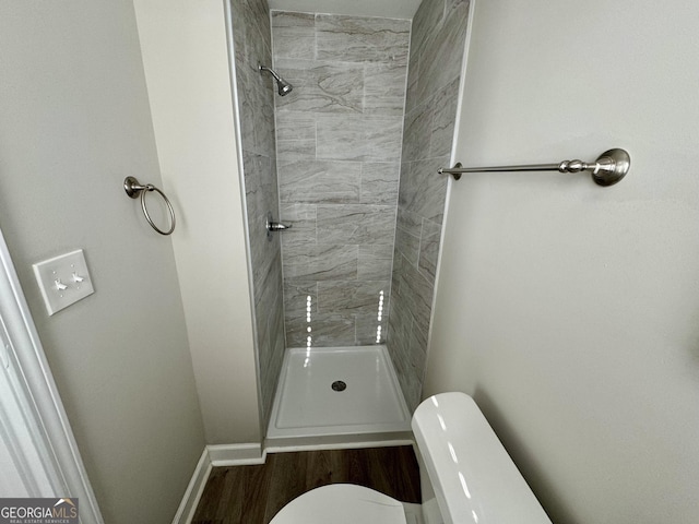 full bath with a tile shower, toilet, and baseboards