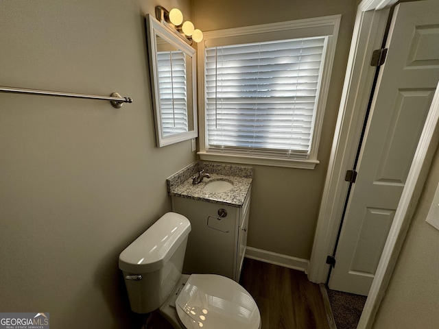 half bath featuring baseboards, vanity, toilet, and wood finished floors