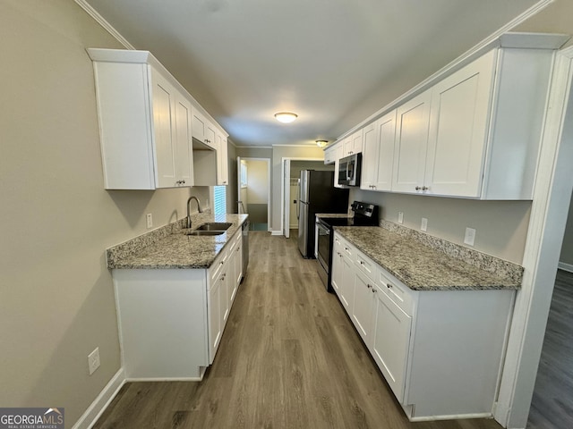 kitchen with stainless steel appliances, wood finished floors, a sink, baseboards, and white cabinets