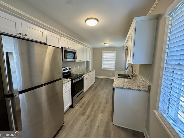 kitchen with light stone counters, appliances with stainless steel finishes, a sink, light wood-type flooring, and baseboards