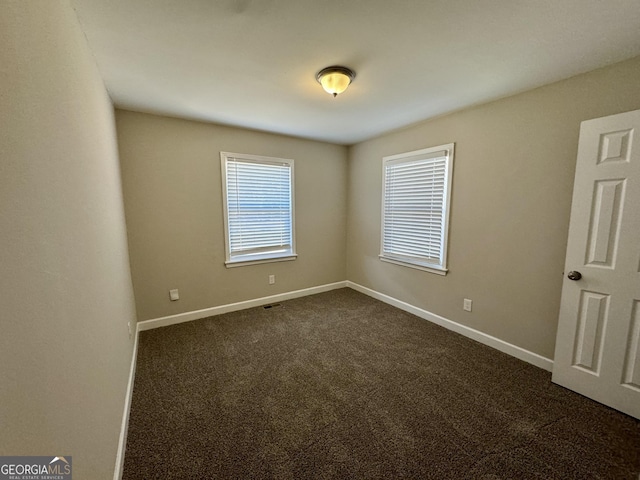 unfurnished room featuring visible vents, dark carpet, and baseboards