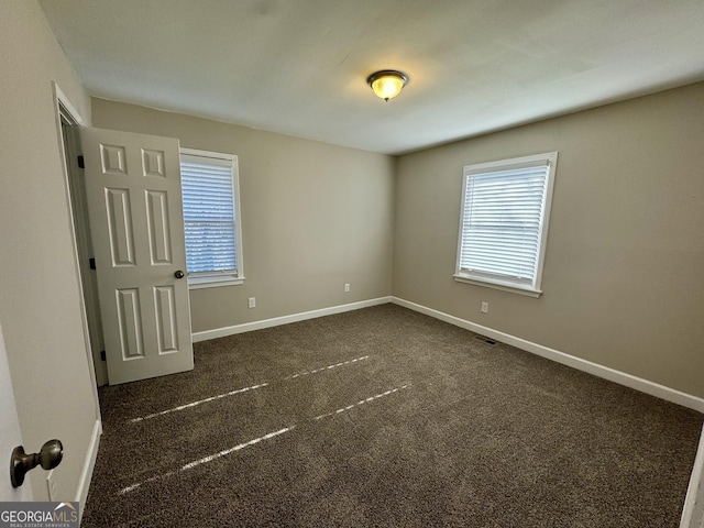 empty room featuring visible vents, dark carpet, and baseboards