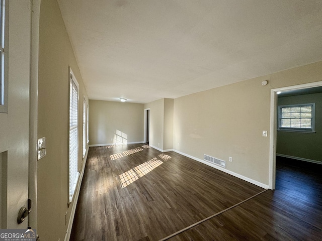 unfurnished room featuring dark wood-style flooring, visible vents, and baseboards