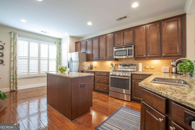 kitchen featuring a center island, visible vents, appliances with stainless steel finishes, a sink, and light stone countertops