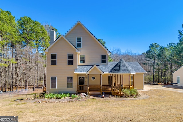 view of front of home featuring covered porch, a shingled roof, a chimney, and a front yard