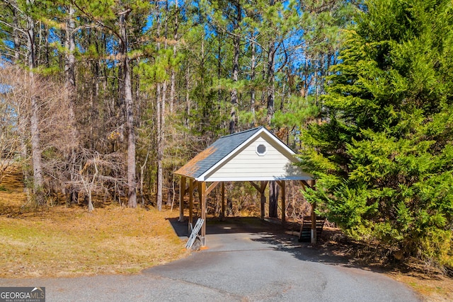 view of car parking with driveway, a wooded view, and a detached carport