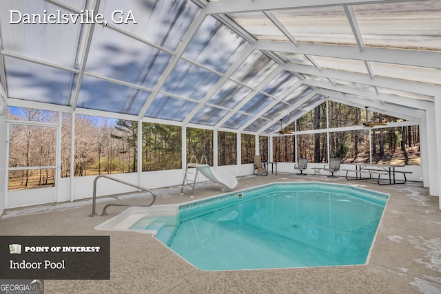 indoor pool with glass enclosure, a water slide, and a patio area