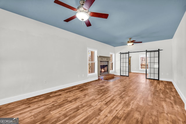 unfurnished living room featuring a barn door, baseboards, ceiling fan, wood finished floors, and a fireplace