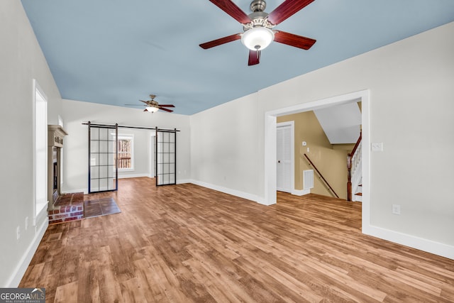 unfurnished living room featuring stairs, a barn door, wood finished floors, and a ceiling fan