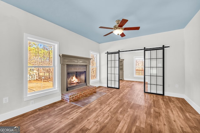 unfurnished living room with wood finished floors, visible vents, a fireplace, and a barn door