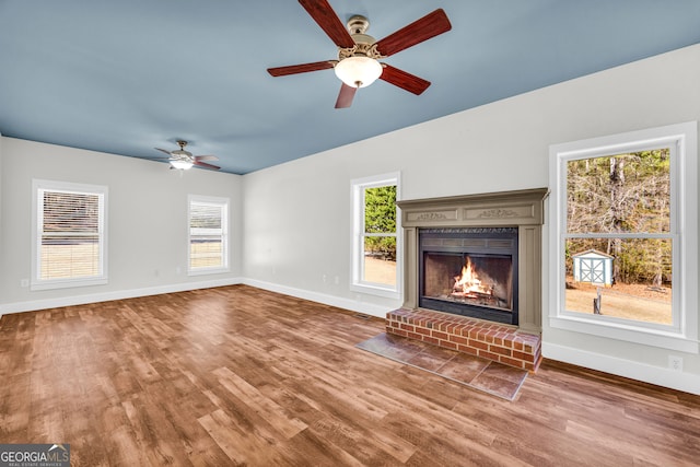 unfurnished living room with a brick fireplace, wood finished floors, a ceiling fan, and baseboards