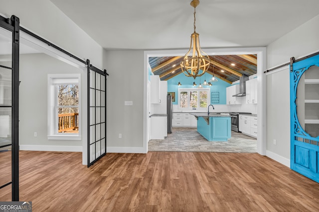 interior space with a barn door, a sink, vaulted ceiling, light wood-style floors, and a notable chandelier