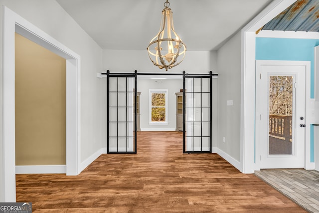 unfurnished dining area featuring a notable chandelier, a barn door, baseboards, and wood finished floors