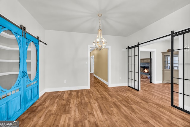 unfurnished dining area featuring an inviting chandelier, a barn door, baseboards, and wood finished floors