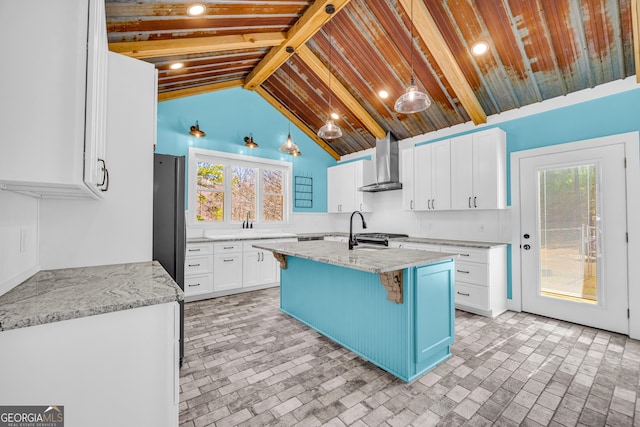 kitchen featuring light stone counters, white cabinets, beamed ceiling, and wall chimney range hood