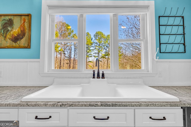 room details with white cabinetry, light countertops, a sink, and wainscoting