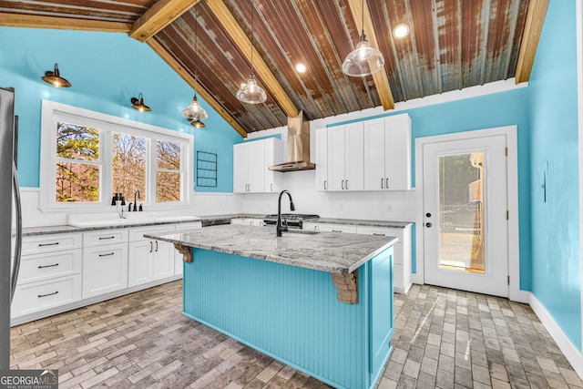 kitchen featuring a kitchen island with sink, white cabinets, light stone countertops, wall chimney exhaust hood, and a kitchen bar