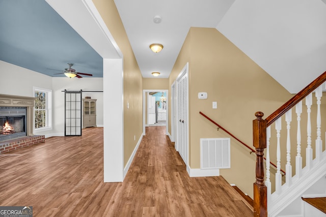 hallway featuring wood finished floors, visible vents, vaulted ceiling, and a barn door