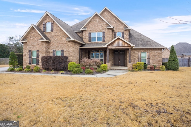 view of front of property with a shingled roof, a front yard, fence, and brick siding