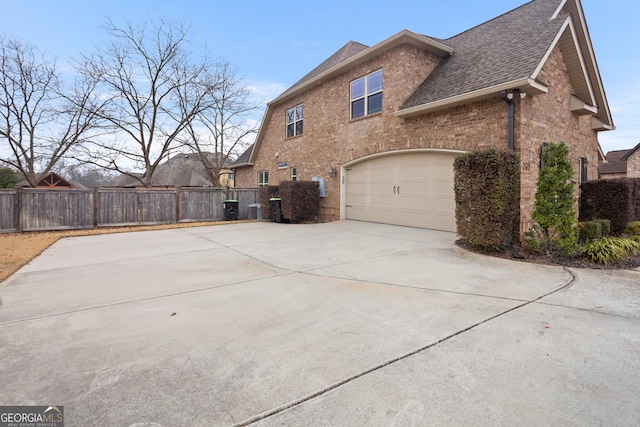 view of property exterior featuring brick siding, roof with shingles, fence, a garage, and driveway