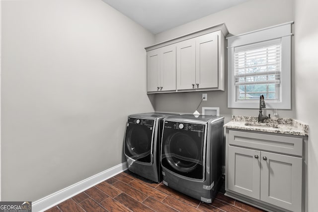 clothes washing area featuring wood finish floors, a sink, baseboards, washer and dryer, and cabinet space